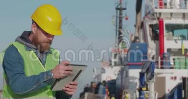 港口<strong>工人</strong>与一个胡子在一个黄色头盔立场与一个平板电脑在海港与船的背景。 <strong>码头工人</strong>
